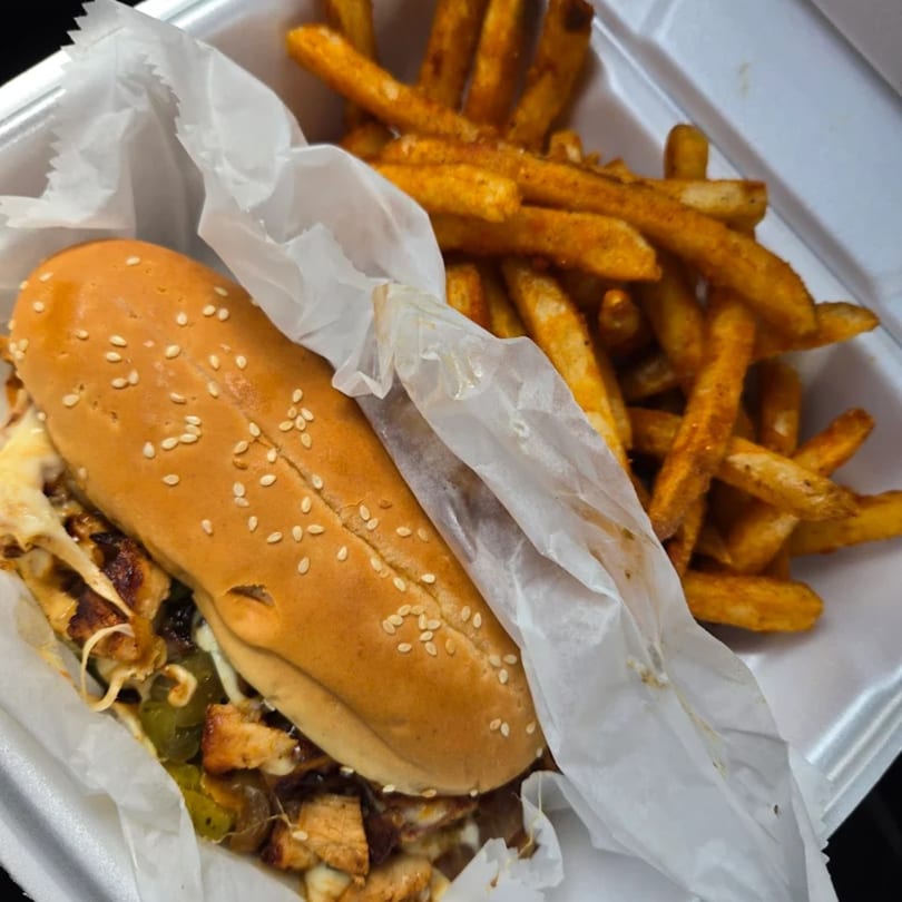 A Burger Shack cheesesteak sandwich with green peppers and onions, served with seasoned fries.