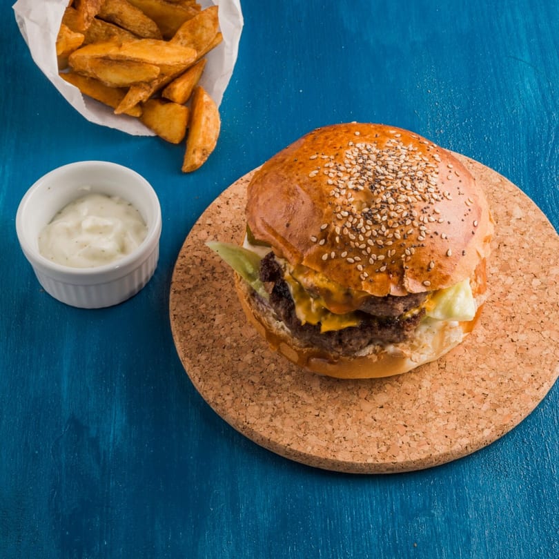 Burger Shack's double cheeseburger with lettuce, sauce, fries, and dip on a blue table.